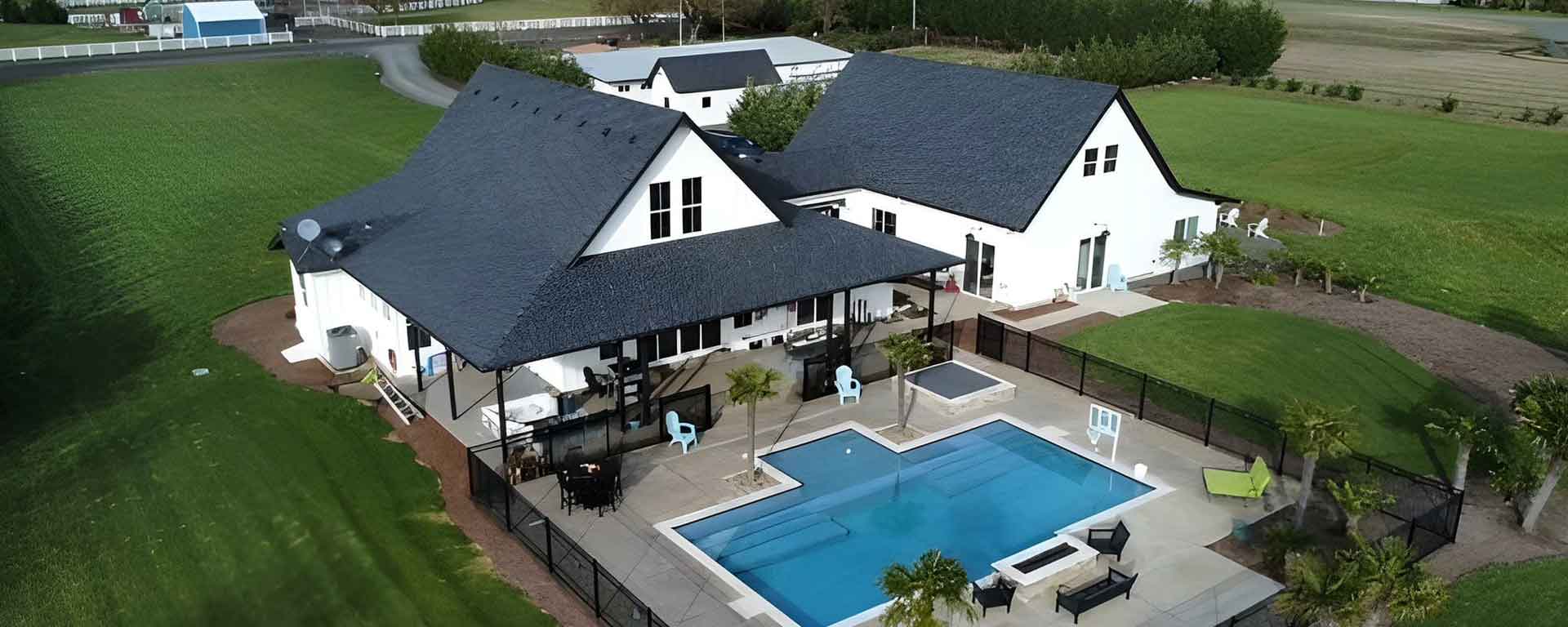 Suburban home with pool and black shingles.