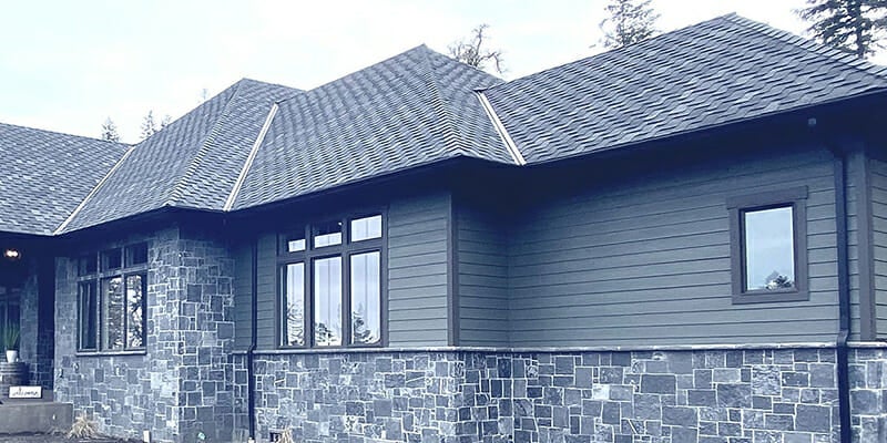 A modern house with dark gray siding, black stone facade, dark asphalt shingles, and dark-framed windows.